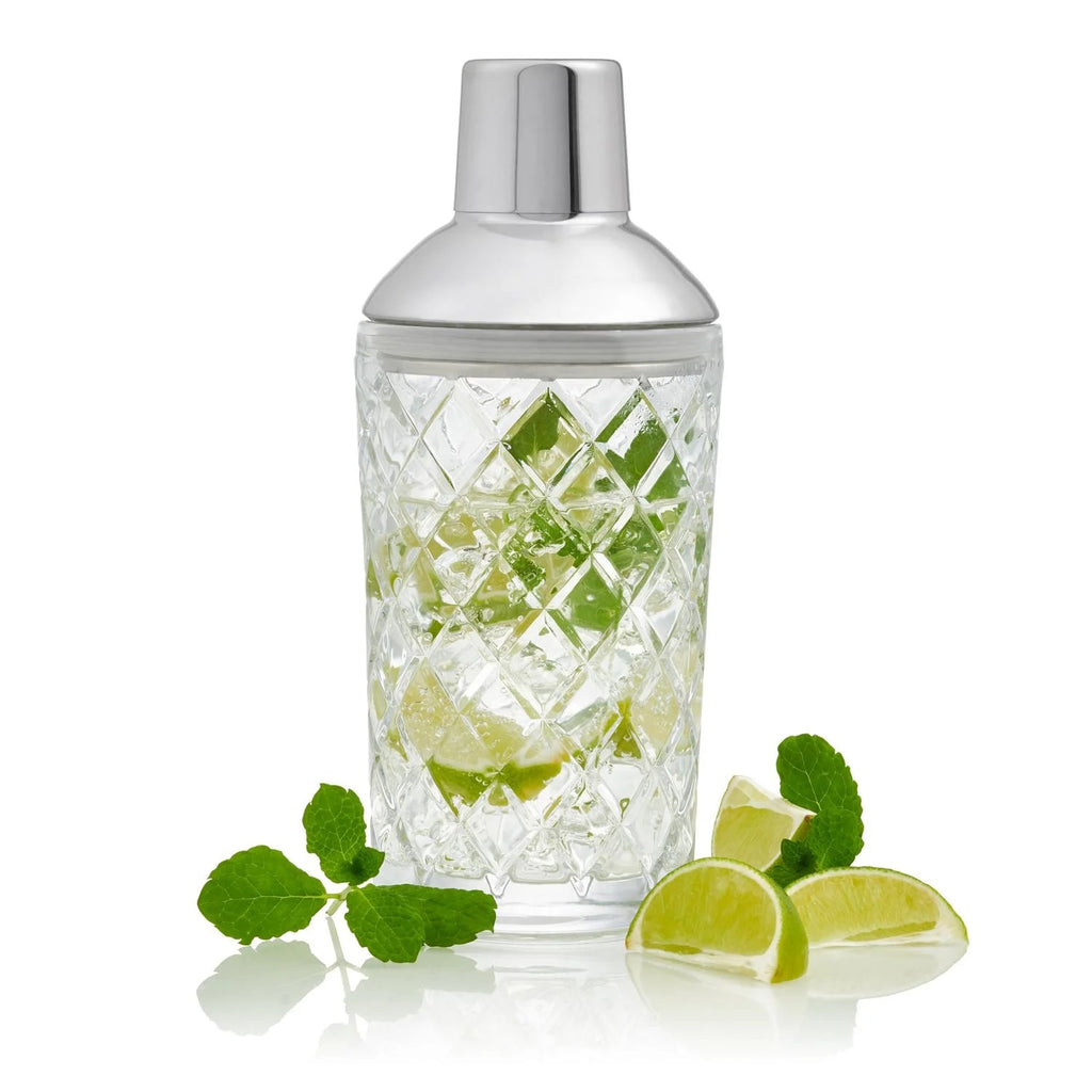 cut glass cocktail shaker with silver top on white background with mint and lime slices