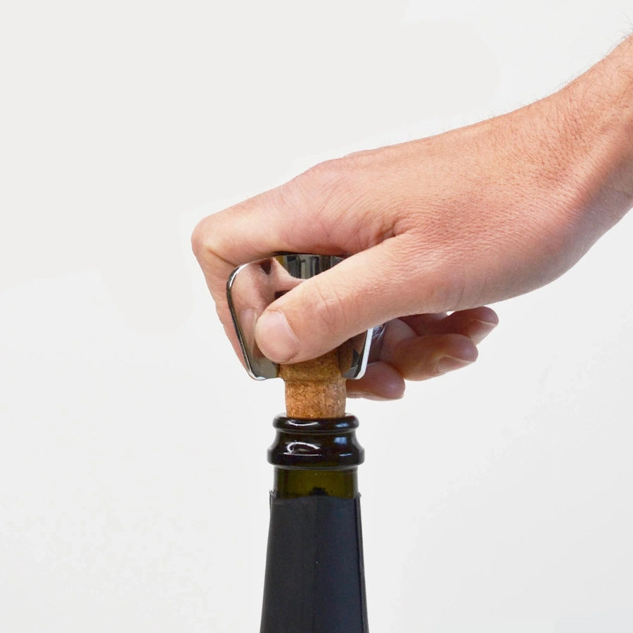 champagne star shaped bottle opener on champagne cork in bottle with hand  on opener using it to remove the cork