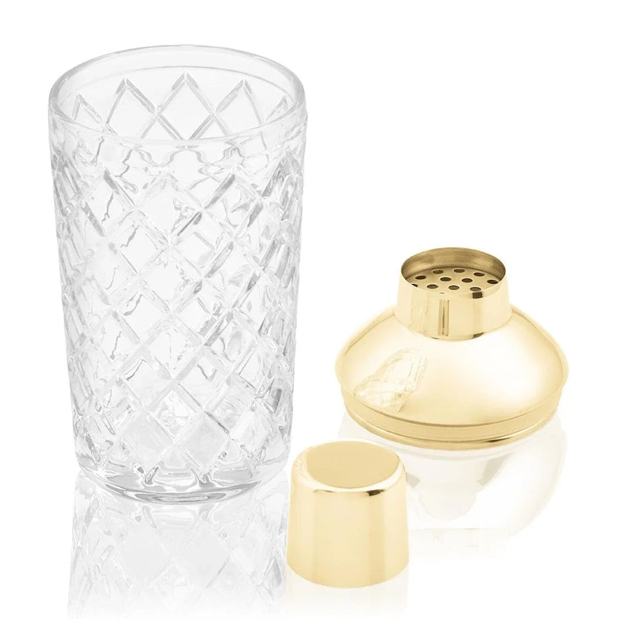 cut glass cocktail shaker on white background  with gold strainer and lid alongside