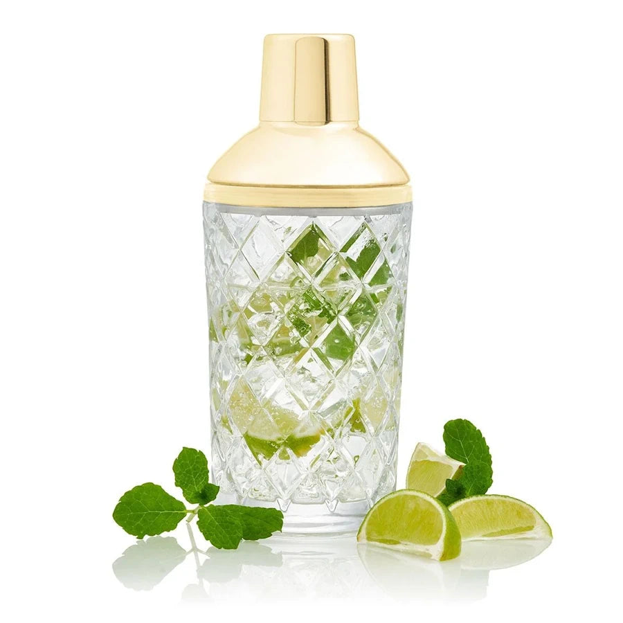cut glass cocktail shaker with gold top on white background with mint and lime slices