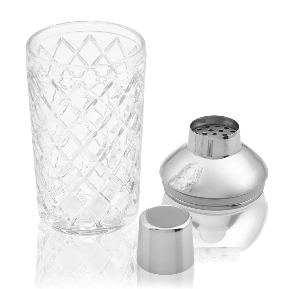 cut glass cocktail shaker on white background  with silver strainer and lid alongside